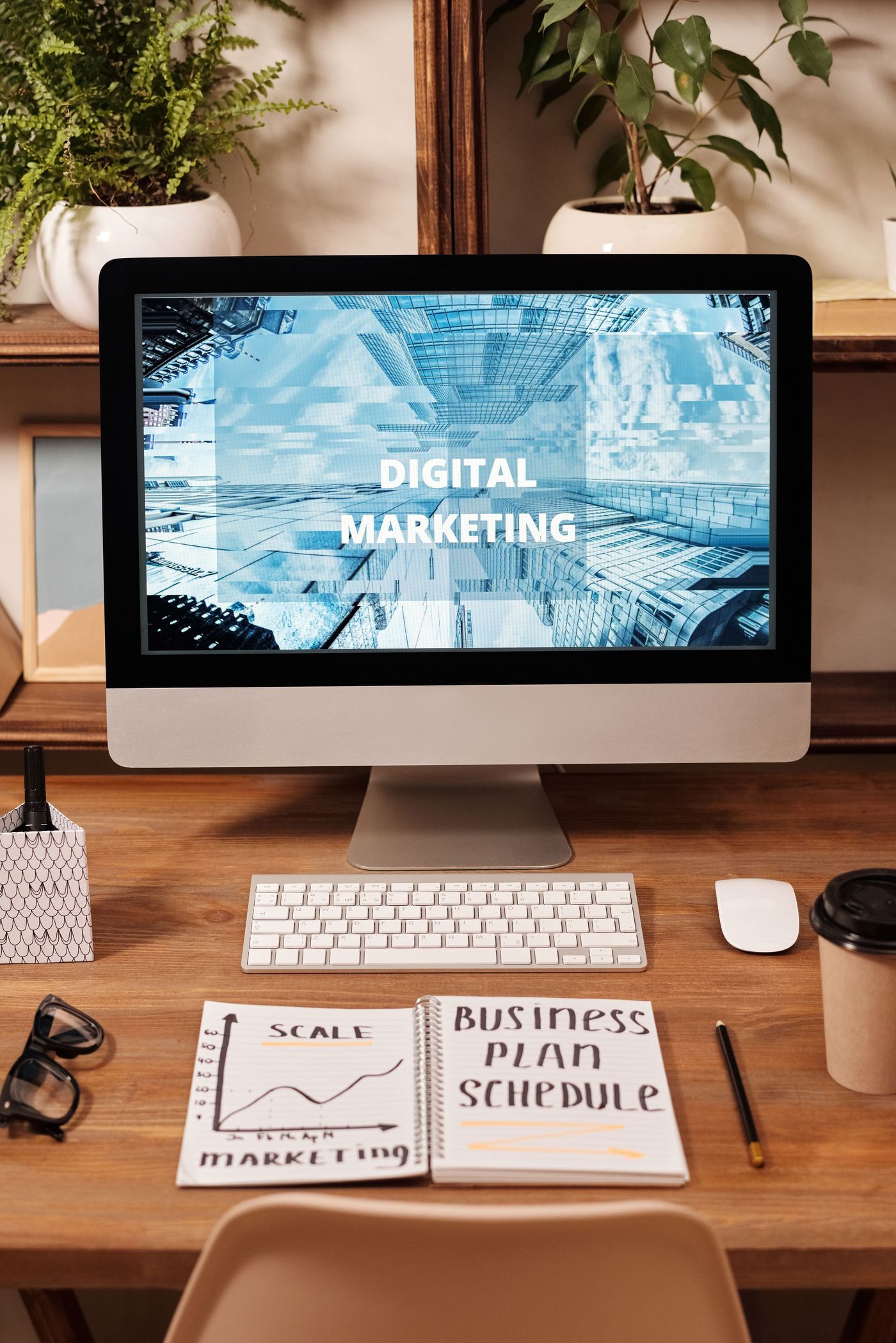 A desk with a digital marketing presentation on screen beside a business plan notebook
